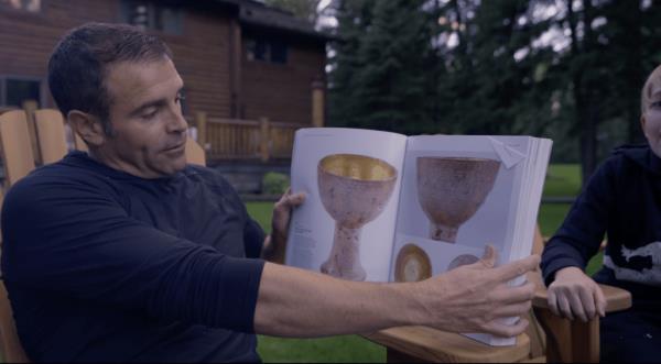 A photo of movie prop collector Tom Biolchini with catalog photos of the Holy Grail cu from 