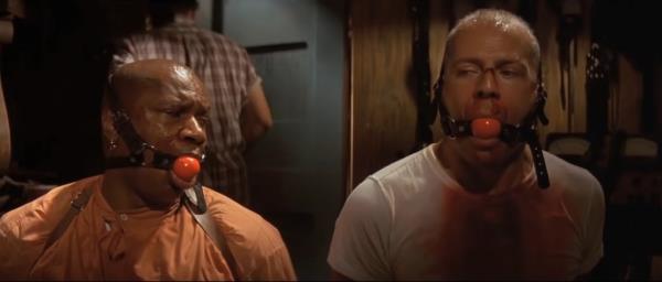 Two men, Ving Rhames and Bruce Willis, tied up with ball gags on their faces in 