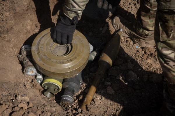 A member of a Ukrainian demining team places unexploded ordnance collected from across the region in a hole in an old crater from an airstrike ahead of destroying it on September 29, 2023