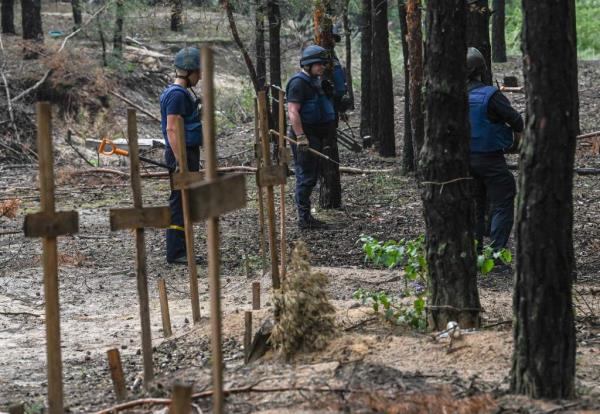 Ukrainian servicemen search for land mines at a burial site in a forest on the outskirts of Izyum, eastern Ukraine on September 16, 2022