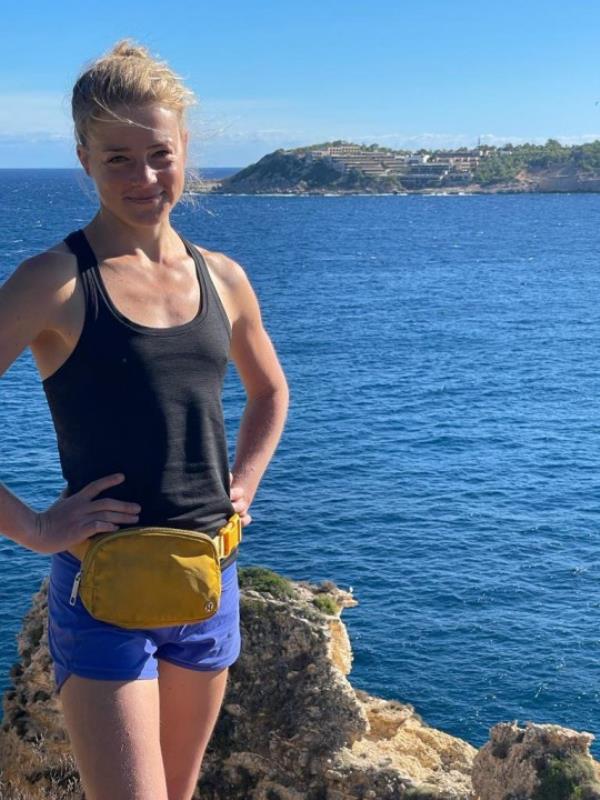 Pandora standing in front of a body of water, wearing a black vest, blue running shorts and a yellow fanny pack.