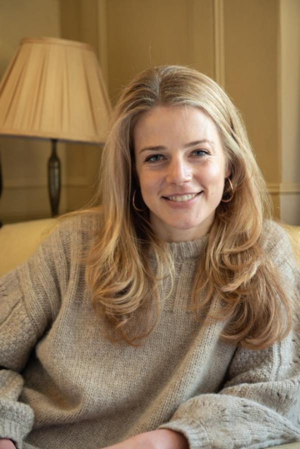 Pandora relaxing on a sofa, she's wearing a light grey jumper, her blo<em></em>nde hair is blow dried and she's smiling to camera