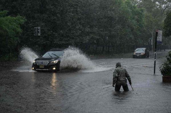Man wades through thigh-high waters during last week's flooding to clear storm drains as car passes, shooting up water alo<em></em>ngside it as it goes through flooded waters.