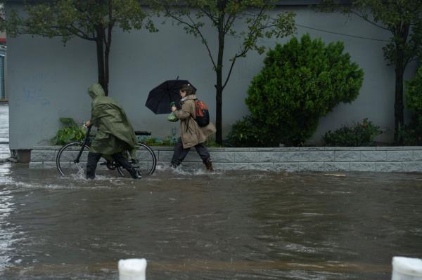 New Yorkers wade through inches of water last week when many parts of the region saw flooding. Person in po<em></em>ncho rolls bike through rain while woman in boots and umbrella wades through water in Brooklyn.