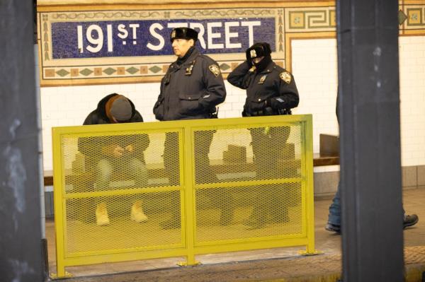 police officers behind a yellow fence near protective barriers in a subway station