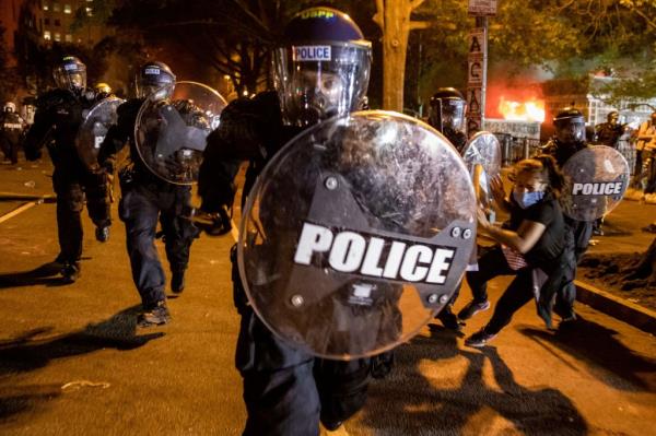 A police officer charges forward as people protest the death of George Floyd at the hands of Minneapolis Police in front of the White House in Washington, DC.