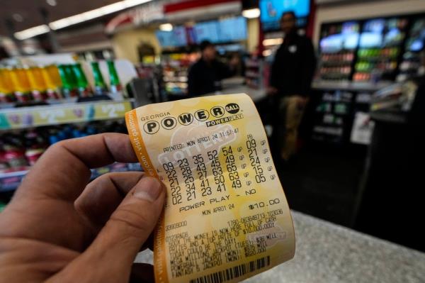 A man's hand holding a Powerball lottery ticket.