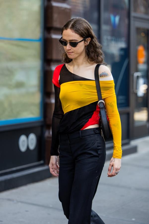 Ella Emhoff wearing a black yellow red striped asymmetric top and black pants walking outside Helmut Lang during New York Fashion Week.