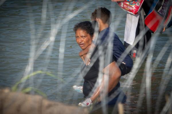  A woman holds a child on her back earlier this mo<em></em>nth as she and other migrants walk along the Rio Grande border with Mexico in Eagle Pass, Texas. 