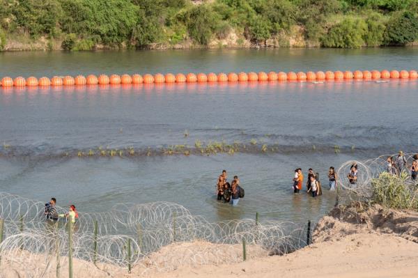 Migrants on July 16 walk past a string of buoys placed on the water along the Rio Grande border with Mexico in Eagle Pass, Texas.