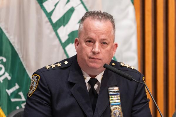 A man in a police uniform standing in front of a podium and micropho<em></em>nes while attending a press briefing in New York City.