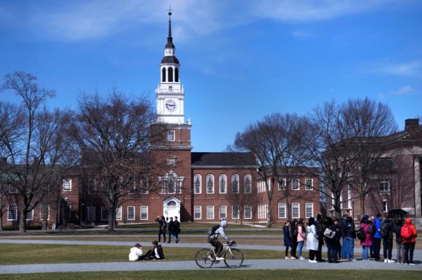 A bicyclist passes a college tour group outside the Baker Library at Dartmouth College, on April 7, 2023.