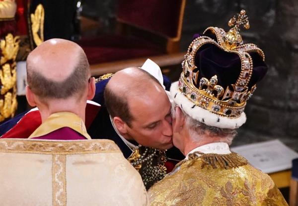 Prince William kissing his father, King Charles III, who is wearing St Edward's Crown, during the coro<em></em>nation ceremony at Westminster Abbey