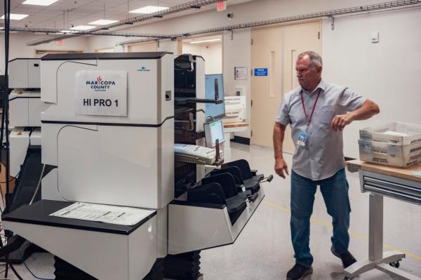 Election worker processing a stack of 2024 General Election ballots using a tabulation machine at the Maricopa County Tabulation and Election Center in Phoenix, Arizona