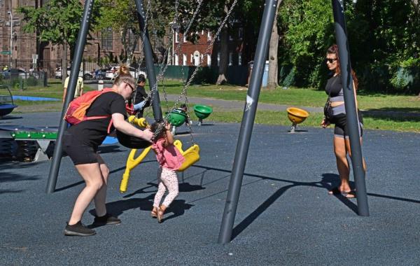 Women push their children on a swingset. 
