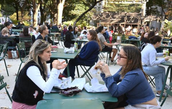 Crowd of people enjoying lunch at tables in Madison Square Park, New York.