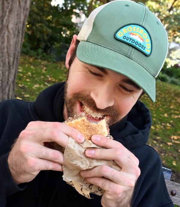 Young man, Co<em></em>nnor Landhauser, happily biting into an expensive prime rib sandwich in Madison Square Park, New York