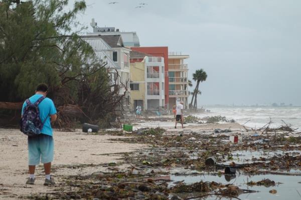 People on the beach amid debris and waves caused by Hurricane Helene.