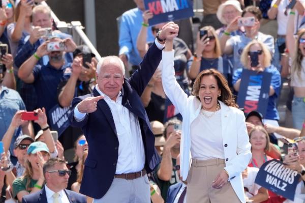 Tim Walz and Kamala Harris holding hands in victory in front of a crowd.