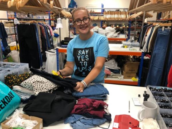 Zara Canfield looking through seco<em></em>ndhand clothes while smiling at the camera.