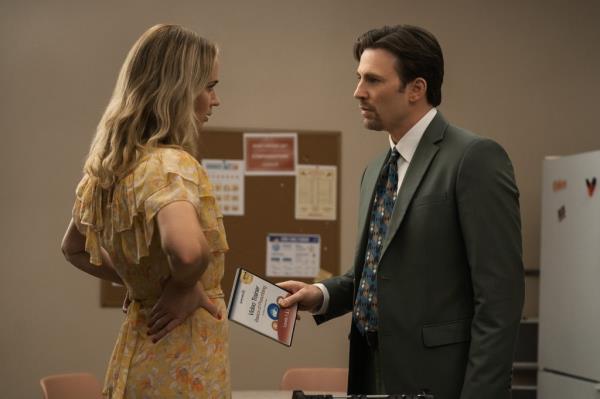 Emily Blunt with her hands on her hips wearing a yellow dress talking to Chris Evans on set of the movie 