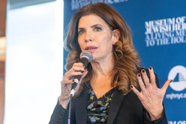 Council member Julie Menin speaking into a microphone at a rally supporting hostages kidnapped by Hamas, surrounded by Holocaust survivors at the Museum of Jewish Heritage