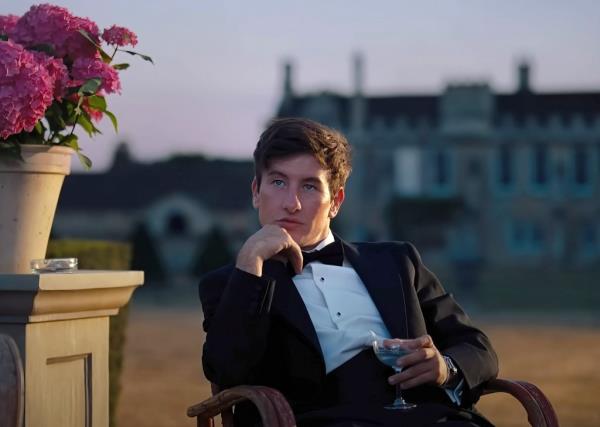 Barry Keoghan in a suit sitting in a chair. 
