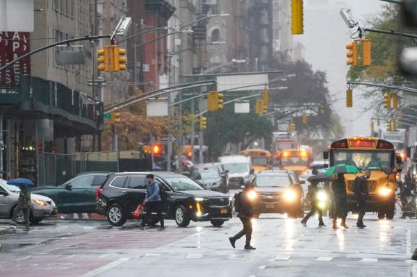 A group of people walking on a wet street with cars during a much-needed rain in NYC, Upper East side
