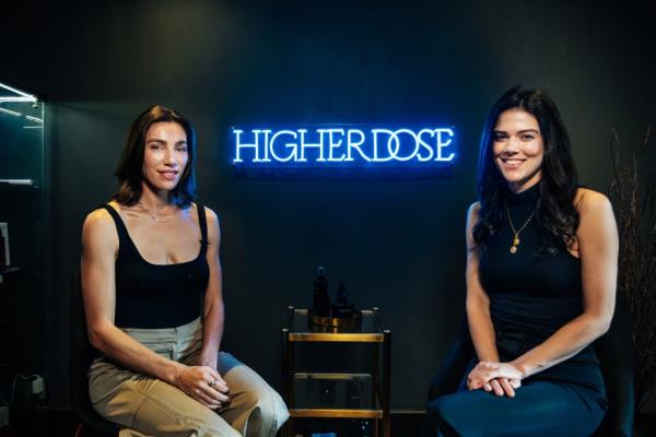 Lauren Berlingeri and Lydia Moynihan sitting in front of a neon sign at the Higher Dose flagship location at the Howard Hotel in Manhattan, photographed by Emmy Park.