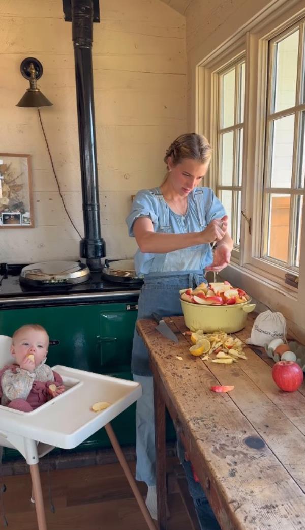Hannah at Ballerina Farm cutting fruit in a kitchen bowl with a baby nearby