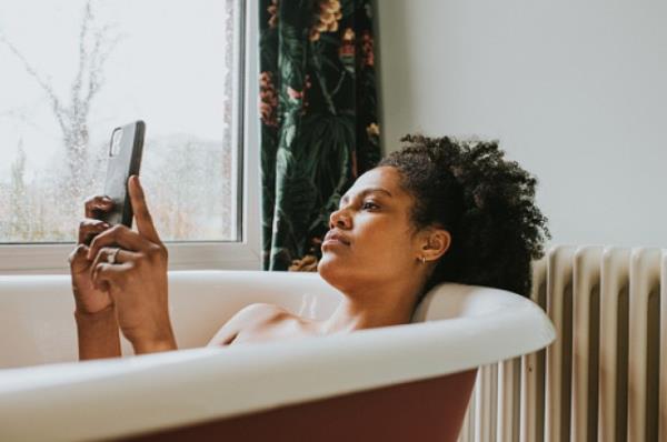 A relaxed woman uses her smart phone as she bathes in a luxurious roll-top bath.